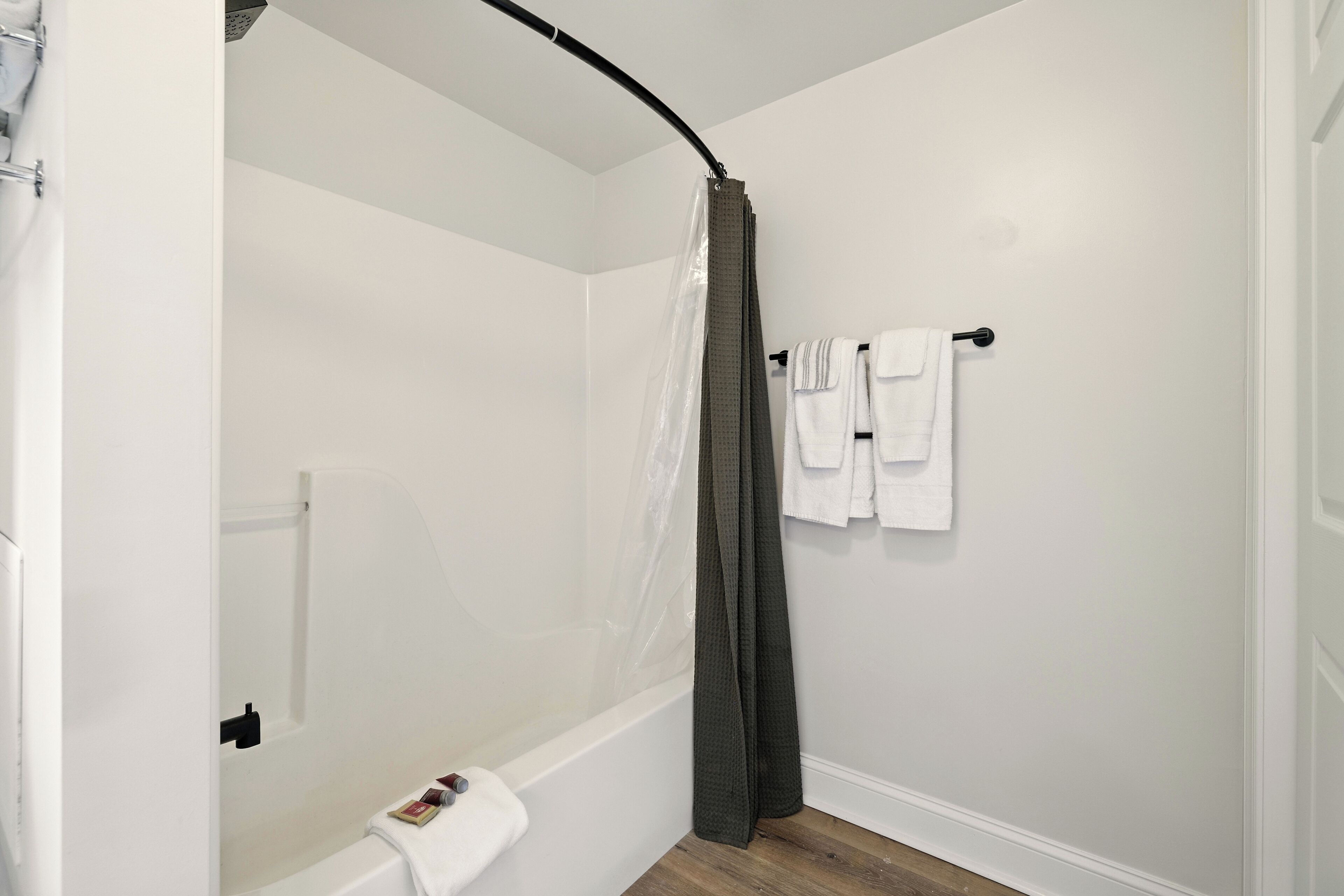 A bathroom with a shower, white walls, and a wooden floor.