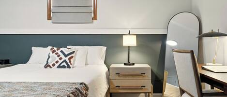A neatly arranged hotel room with a bed, bedside table, lamp, chair, and a mirror.