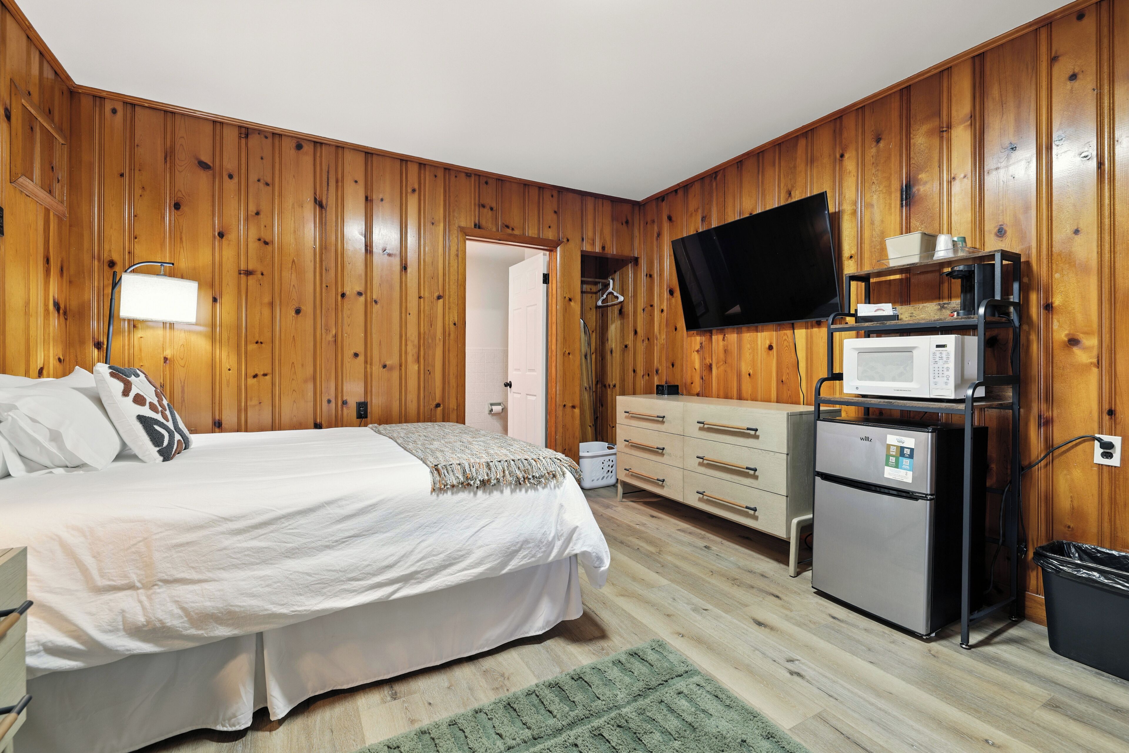 A bedroom with a bed, dresser, TV, microwave, and refrigerator.