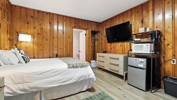 Un dormitorio con cama, cómoda, televisor, microondas y refrigerador.