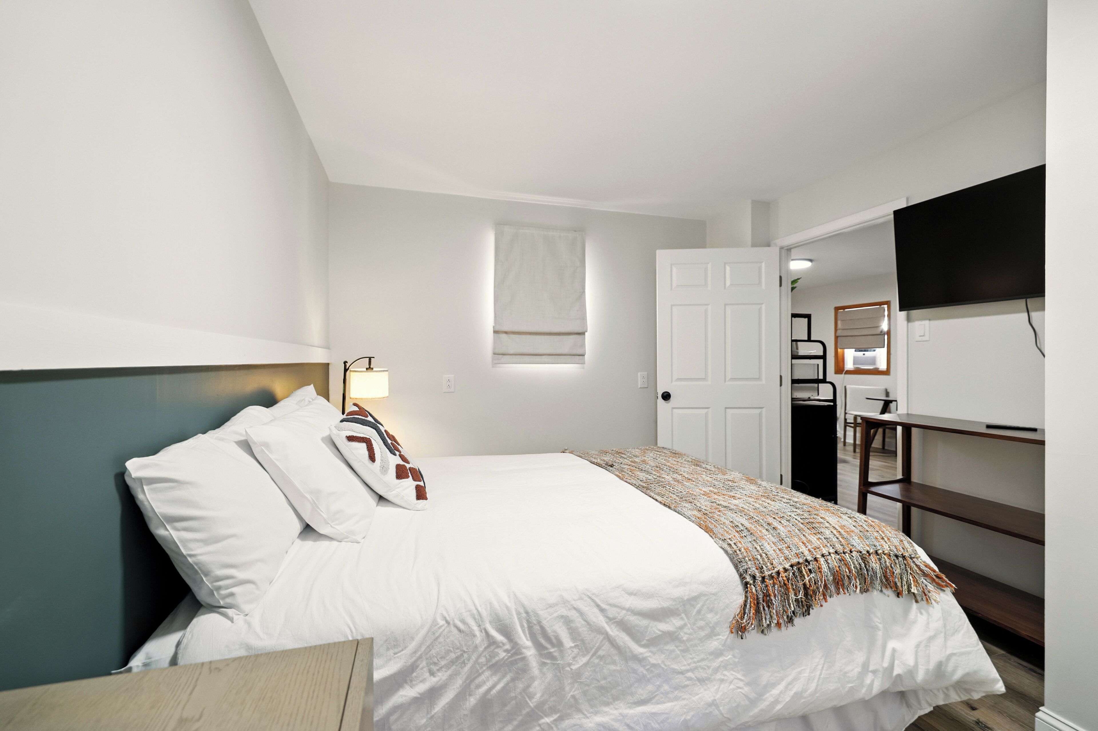 A bedroom with a bed, a bedside table, a lamp, a wardrobe, and a television mounted on the wall.