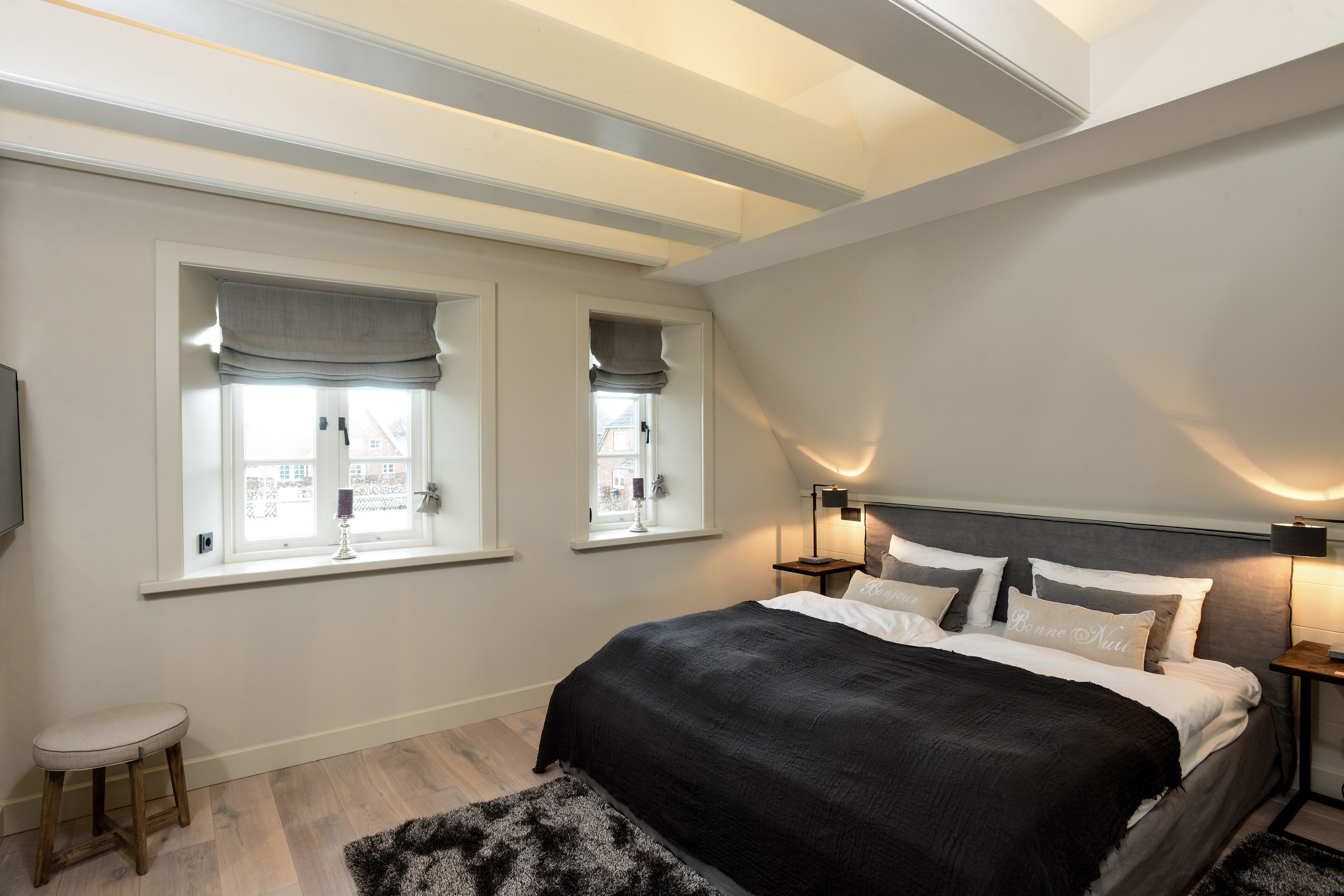 Une chambre avec un grand lit, deux tables de chevet, un petit tabouret et une fenêtre donnant sur un beau paysage.