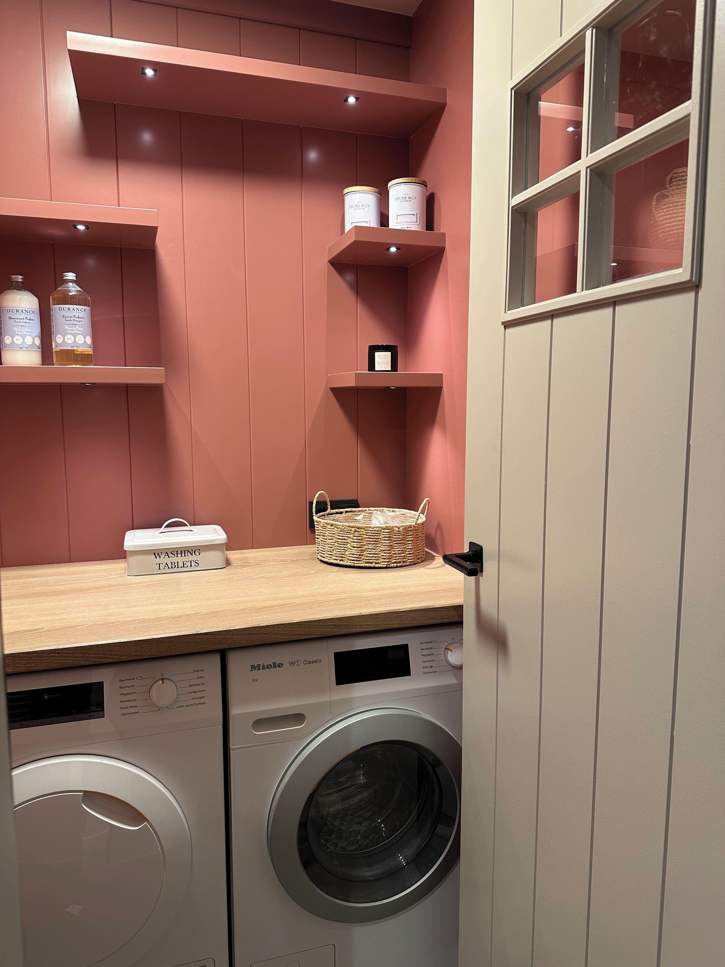 Un espace buanderie comprenant un lave-linge, un panier à linge et des étagères de rangement pour les articles de toilette.