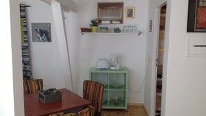 Una cocina compacta con zona de comedor, que incluye una cafetera, un estante verde con utensilios de cocina y un cuadro enmarcado sobre el estante.