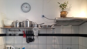 Una cocina con un lavamanos, estufa y diversos utensilios. Hay un reloj en la pared y una planta en maceta sobre la encimera.