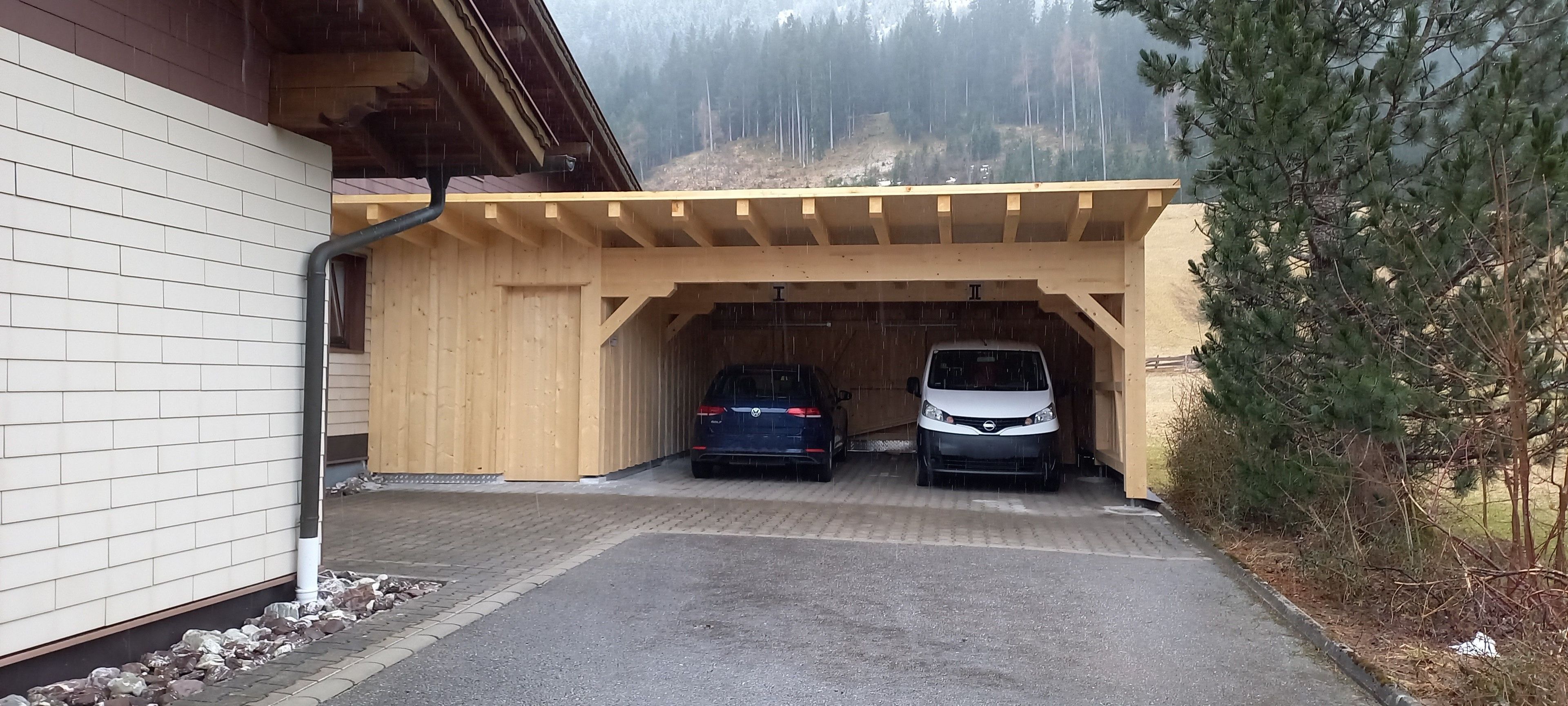 Un espace de stationnement couvert pouvant accueillir deux voitures, une structure en bois et un bâtiment aux murs en briques blanches.