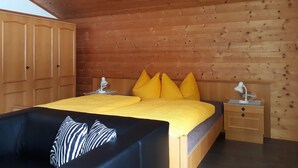 Ein Schlafzimmer mit Holzbalkendecke, einem Bett mit gelben Kissen, einem schwarzen Sofa und einem Nachttisch mit Lampe.