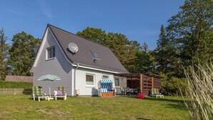 Une maison à deux étages, dotée d’un toit en pente, d’une antenne parabolique et d’un patio couvert aménagé avec du mobilier d’extérieur.