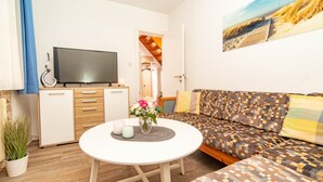 Un salon moderne avec un canapé, un téléviseur, une petite table sur laquelle est posé un vase de fleurs et une plante en pot.