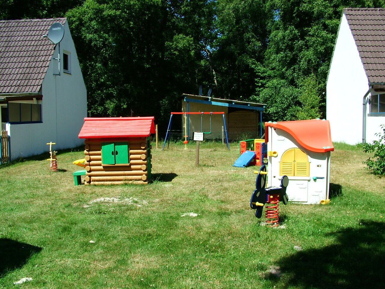 Een speeltuin met een schommel, een klein houten poppenhuis en een glijbaan.