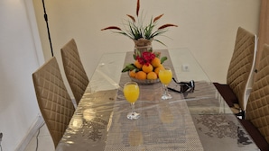 Un tavolo da pranzo con sedie, un vaso con fiori e una ciotola di frutta.