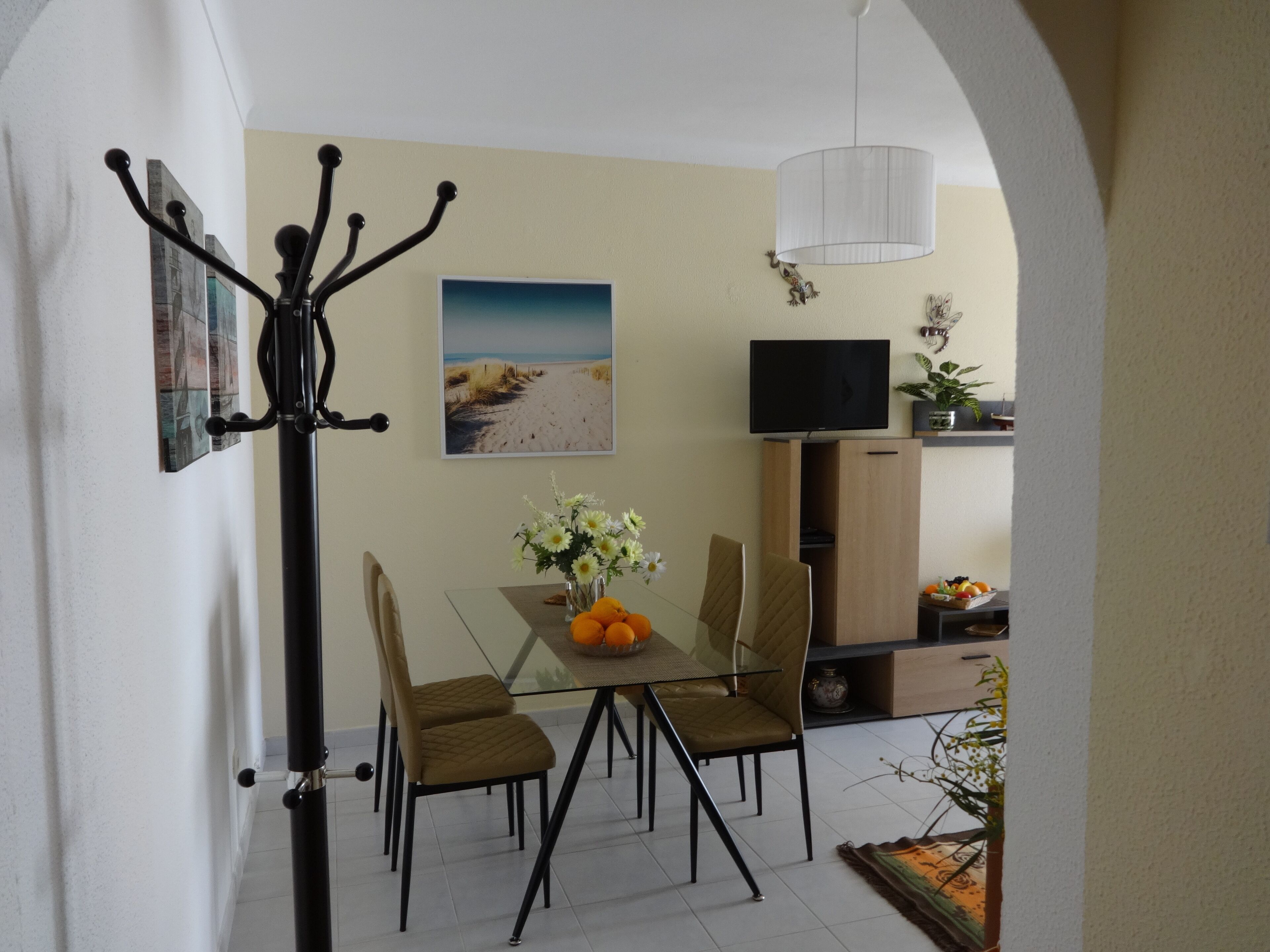 A dining area with a glass table, two chairs, a vase of flowers, and a painting on the wall.