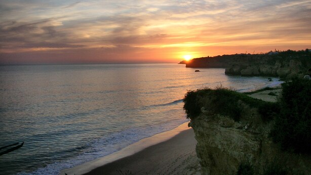 Tramonto sulla costa con spiaggia e scogliere.