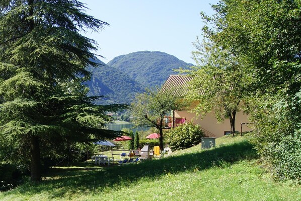 Une vue sur une colline, avec une montagne en arrière-plan, un bâtiment avec un toit rouge et des tables à l’extérieur, protégées par des parasols.