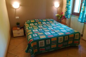 Une chambre à coucher avec un lit recouvert d’une courtepointe aux couleurs vives, une table de chevet ornée d’une plante et une fenêtre avec des rideaux.
