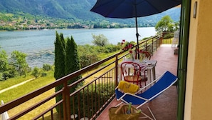 Een balkon met uitzicht op een meer en bergen, met buitenmeubilair en een tafel met stoelen.