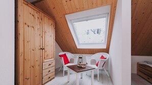 A room with a sloped ceiling, wooden wardrobe, white wicker chairs, a small table, and a skylight.