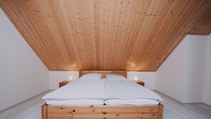 A wooden bed with a sloped ceiling in a room with white walls and floors.