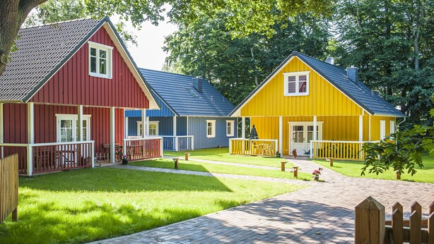A row of colorful wooden cabins with a grassy yard and a wooden deck.