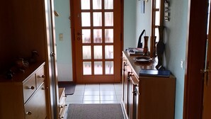 A narrow hallway with a wooden cabinet, a tiled floor, a door with frosted glass panels, and a small rug.