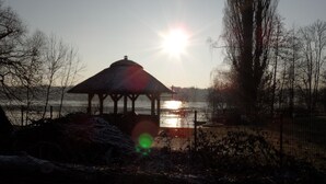A gazebo by a lake with the sun low on the horizon.