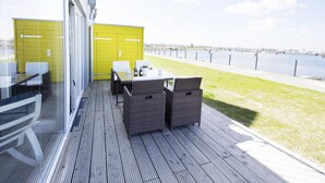 A deck with wicker furniture and a yellow storage unit, overlooking a body of water. - Ostseeliebe - Ground Floor, waterfront, Terrace, Whirlpool Bath, Infrared Sauna (Olpenitz)