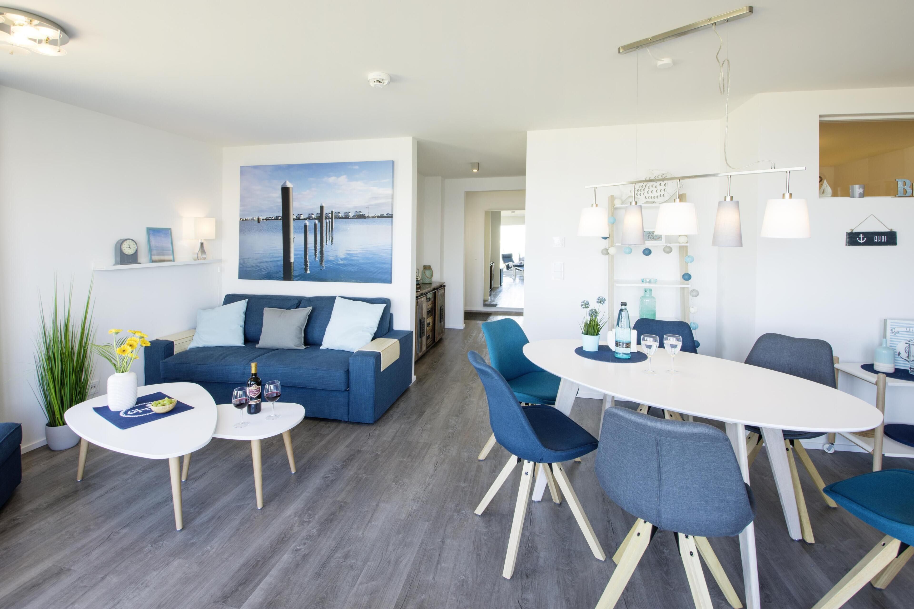 Una sala de estar moderna con un sofá azul, una mesa de comedor con sillas y un cuadro grande de un muelle.