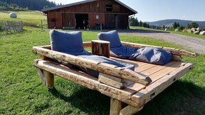 A wooden bench with cushions in a grassy area with a barn in the background. - A place in the sun in the Black Forest, for hiking, relaxing and enjoying (Ühlingen- Birkendorf)