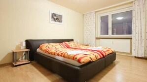 Een slaapkamer met een bed, nachtkastje, raam met gordijnen en een radiator.