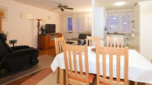 Een woonkamer met een eettafel, stoelen, een bank, een televisie en een plafondventilator.