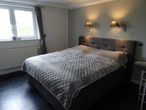 Ein Schlafzimmer mit einem großen Bett, zwei Wandleuchten, einem Heizkörper und einem Fenster mit Vorhängen.