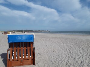 Ein Strand mit einem hölzernen Stuhl, der mit einer blauen Plane abgedeckt ist, feinem Sand und ruhiger See.