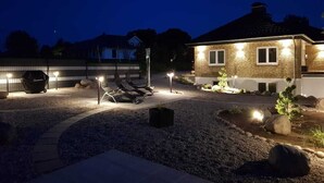 A well-lit outdoor area with a barbecue grill, lounge chairs, and a landscaped garden at dusk. - Weissenhäuser Strand Ostsee Holiday house with high equipment (Wangels)