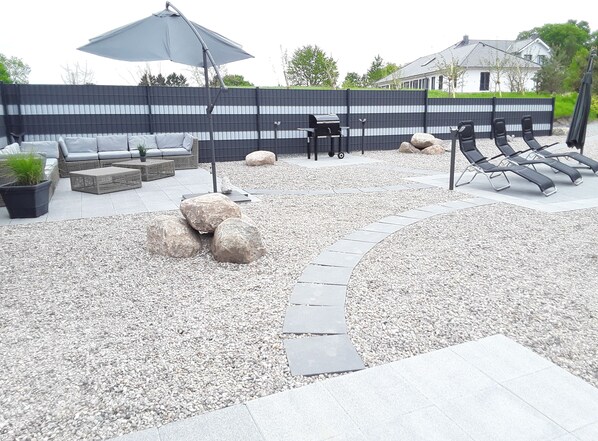 Eine Terrasse mit Gartenmöbeln, einem Grill und einer Zierfelsanordnung.