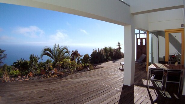 A wooden deck with a view of the ocean, a covered outdoor seating area, and a modern building structure. - HOLIDAYS WITH VISION AND --RUHIG ENTSPANNEND-- COMFORTABLE AND QUALITY  (Tijarafe)