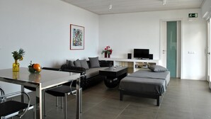 A modern, well-lit room with a dining table, sofa, and a bed. There is a TV on a stand and a vase with flowers on the wall. - HOLIDAYS WITH VISION AND --RUHIG ENTSPANNEND-- COMFORTABLE AND QUALITY  (Tijarafe)
