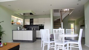 Una cocina moderna con gabinetes blancos, una isla central y un comedor con sillas blancas.