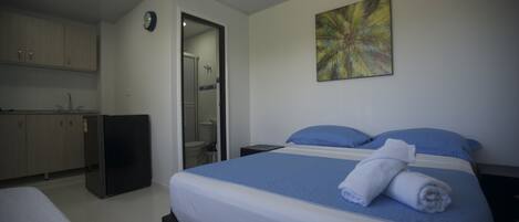 Een hotelkamer met een bed, een klein bureau, een spiegel, een kledingkast en een badkamer die door een open deur zichtbaar is.