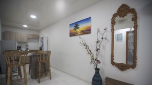 Un coin repas avec des chaises en bois, un vase de fleurs, un tableau représentant un coucher de soleil et un miroir au mur.