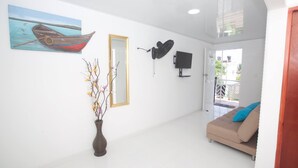 Un vaste espace de vie agrémenté d’un grand tableau représentant un bateau, d’un miroir, d’un ventilateur fixé au mur et d’un téléviseur.