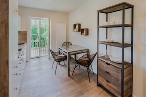 Uma área de refeições com mesa de vidro, duas cadeiras, um armário de madeira e uma estante de metal.