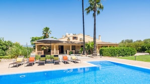 Une piscine avec des chaises longues, une maison avec un toit en tuiles et des palmiers.