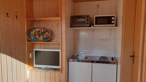 Una cucina compatta con pareti in legno, un forno a microonde, un tostapane, un lavandino e un televisore su uno scaffale.