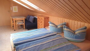 Una camera da letto mansardata accogliente, con soffitto spiovente, una scrivania in legno, un divano e un letto con copriletto a righe.
