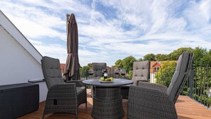 Una terraza en la azotea con mobiliario de mimbre, una mesa con fruta y una botella de vino.