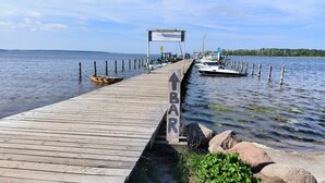 Un muelle de madera que conduce a un embarcadero con barcos, un cartel y vistas al agua.