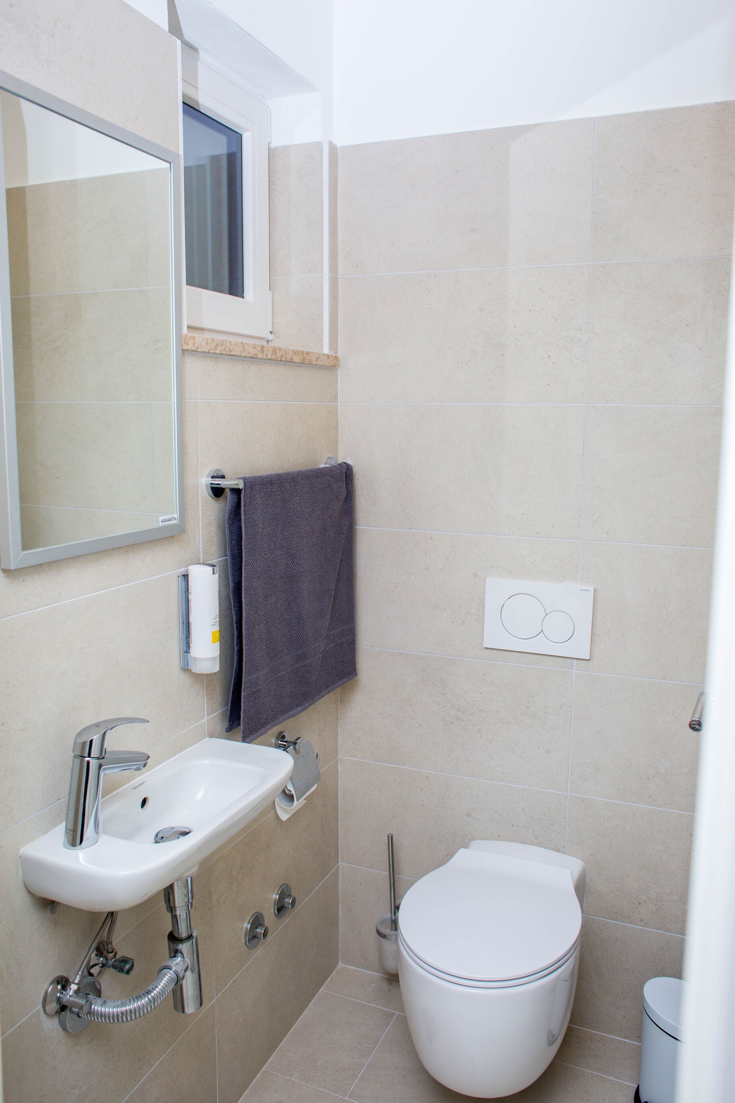 A bathroom with a sink, mirror, towel, toilet, and a window.