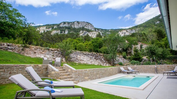 A pool area with lounge chairs, a stone wall, and a mountainous backdrop. - Luxury wellness villa in a quiet area of Northern Istria (Lanišće)