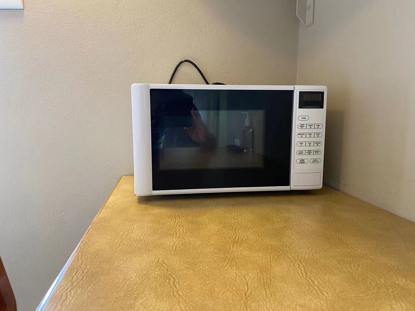 Un microondas blanco sobre una mesa de madera en una habitación con paredes lisas.