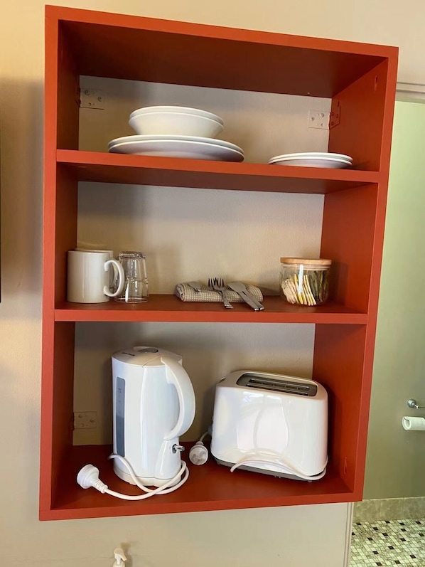 A kitchen shelf with white plates, a coffee mug, a glass, a jar, a kettle, and a toaster. - Apollo Motel Parkes (Parkes)